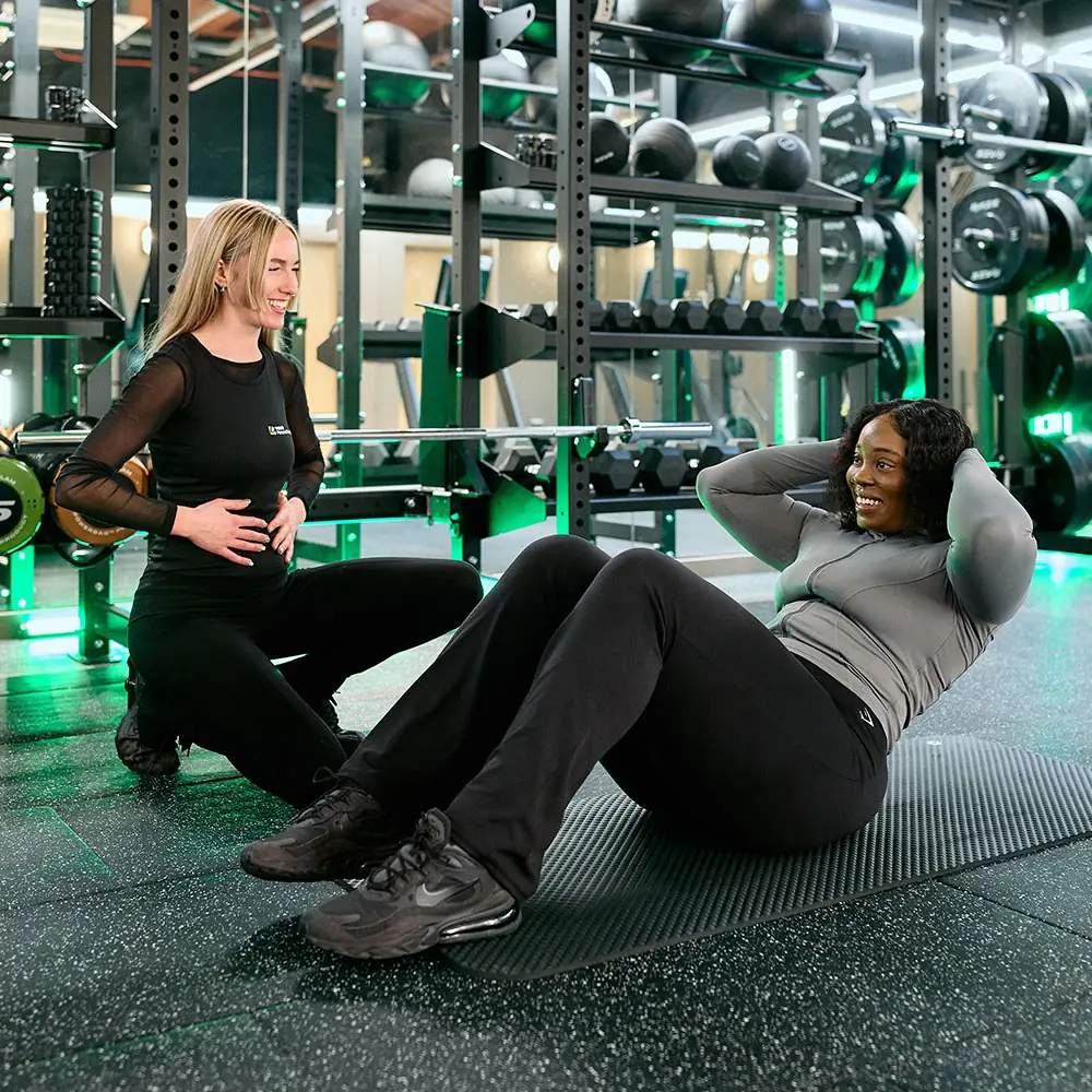 A YOUR Personal Training trainer on the gym floor coaching a member through sit-ups on a mat